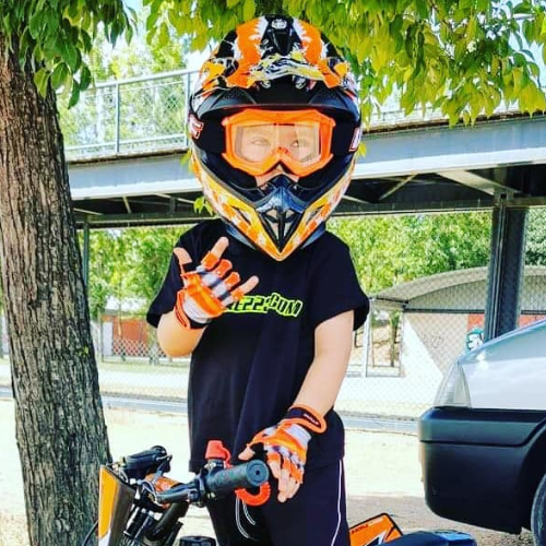 Boy sitting on a black and orange quad bike, wearing a orange wulfsport helmet and googles