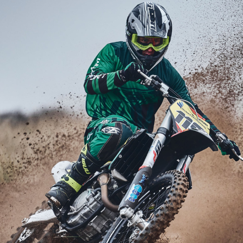 Man riding a motorcross bike, wearing a green wulf sport suit and helmet.