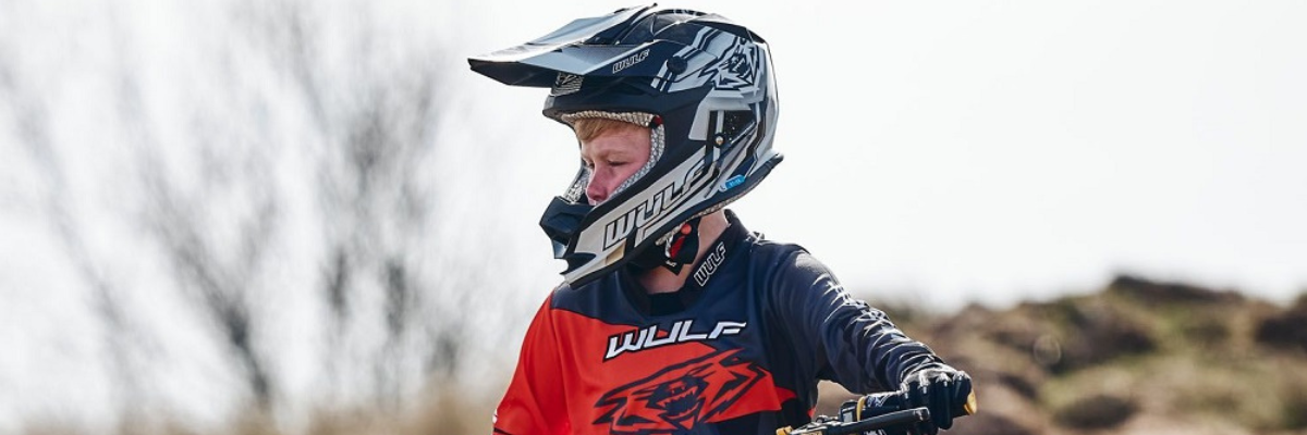 Young boy wearing a black and silver wulfsport helmet and wulfsport suit