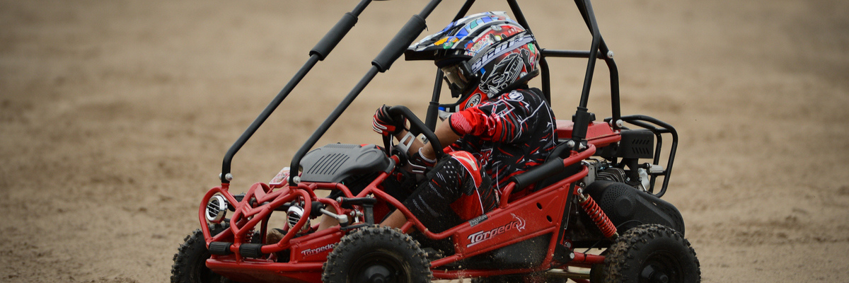 Child driving a red hammerhead torpedo kids off road buggy on dirt track